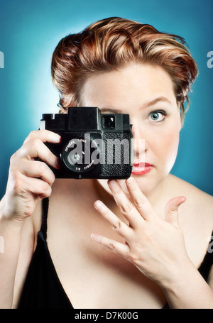 Portrait of young woman taking a picture with a toy camera in studio against blue backdrop