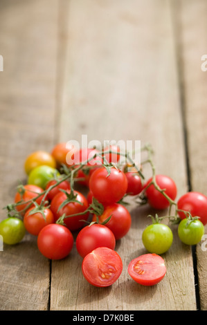 Close up of a string of vine-ripe cherry tomatoes on a rustic wooden tabletop. Stock Photo