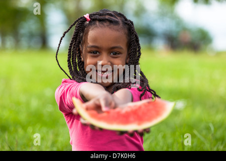 Outdoor portrait of a cute young black little girl eating watermelon - African people Stock Photo