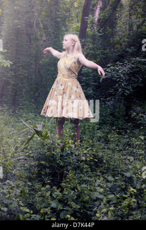 a blond girl with a yellow dress is dancing in the woods Stock Photo