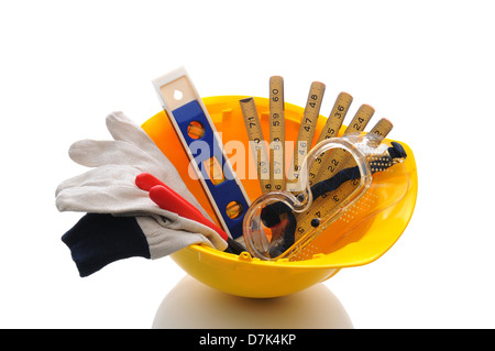 A yellow contractors hard hat with work gloves and tools inside. Horizontal format over white with reflection. Stock Photo