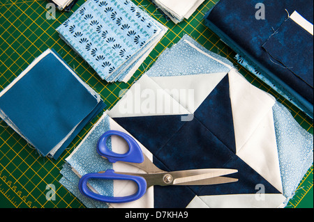 Quilting or patchwork materials and tools on a green measuring board with scissors showing blue and white patterned fat quarters Stock Photo