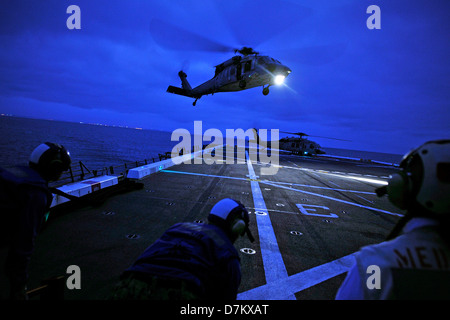 A US Navy MH-60S Seahawk helicopter approaches the flight deck of the amphibious transport dock ship USS New Orleans during night flight operations April 30, 2013 in the Pacific Ocean. Stock Photo