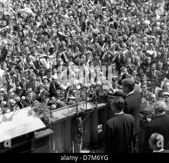 The US president John F. Kennedy (right, at the lectern, waving) and the governing Mayor Willy Brandt (to his left) are standing on front of the city hall Schöneberg of West Berlin, where tens of thousands of people cheer Kennedy.