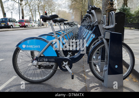 Boris bikes on Embankment London lined up waiting to be hired with black cab taxis and traffic in the background Stock Photo