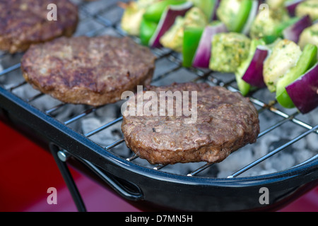 Burgers on BBQ - Patties being grilled on a portable barbeque outdoors. Chicken kebabs on background. Stock Photo