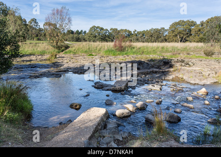 tranquil creek flowing over rocks with broken miniature dam. Stock Photo