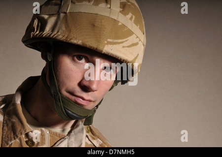 Portrait of a soldier with  blank expression on his face against a dark background. Soldier is wearing British Military uniform. Stock Photo