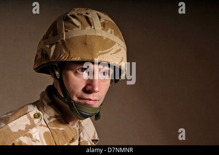 Portrait of a soldier with  blank expression on his face against a dark background. Soldier is wearing British Military uniform. Stock Photo