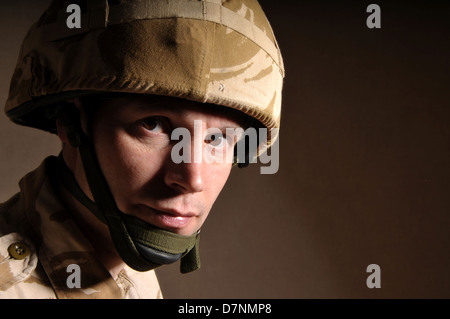 Portrait of a soldier with  blank expression on his face against a dark background. Soldier is wearing British Military uniform. Stock Photo