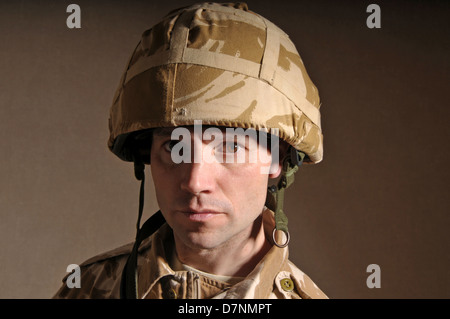 Portrait of a soldier with  blank expression on his face against a dark background. Soldier is wearing British Military uniform. Stock Photo