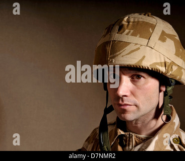 Portrait of a soldier with  blank expression on his face against a dark background. Soldier is wearing British Military uniform. Stock Photo