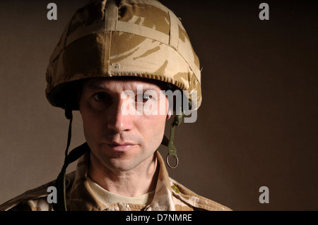 Portrait of a soldier with  blank expression on his face against a dark background. Soldier is wearing British Military uniform. Stock Photo