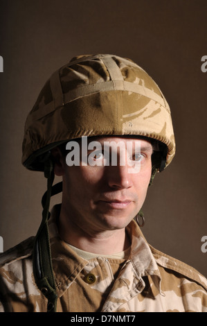 Portrait of a soldier with  blank expression on his face against a dark background. Soldier is wearing British Military uniform. Stock Photo