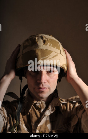 Portrait of a soldier with  blank expression on his face against a dark background. Soldier is wearing British Military uniform. Stock Photo