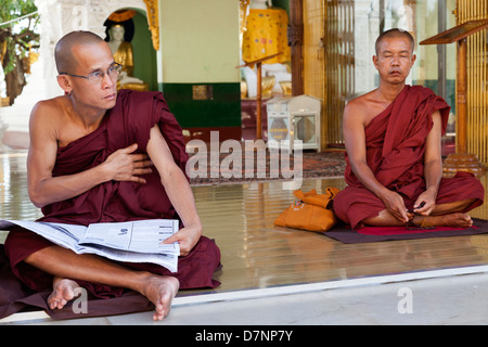 Two monks - one meditating and one reading a newspaper - at the Shwedagon Pagoda in Yangon, Myanmar Stock Photo
