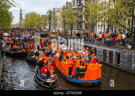 Annual Queens Day in The Netherlands. Boat parade in the canals of Amsterdam, old town. People dressed in orange. Amsterdam Stock Photo