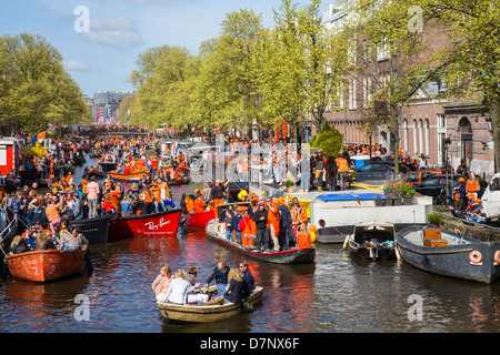 Annual Queens Day in The Netherlands. Boat parade in the canals of Amsterdam, old town. People dressed in orange. Amsterdam Stock Photo