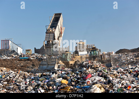 Landfill, tractor compactors pushing trash.  Tipper dumping semi trailer containing collected garbage. Stock Photo