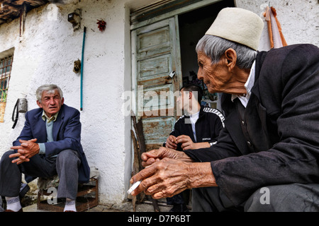 Qamile Stema one of the last 'Sworn Virgins' of Albania, smoking and sitting at her house entrance with some of the village men Stock Photo