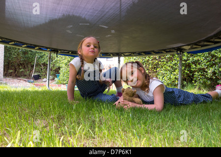 Sisters, aged 3 and 4, playing happily underneath a trampoline in the garden. Stock Photo