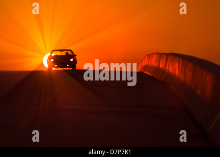 Car Silhouette And Sun At Sunset On Highway With Sunburst, USA Stock Photo