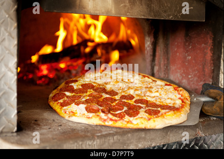 A pepperoni pizza cooks in a wood fired pizza oven. Stock Photo