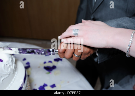 Bride and groom on wedding day cutting cake closeup showing rings and knife Stock Photo