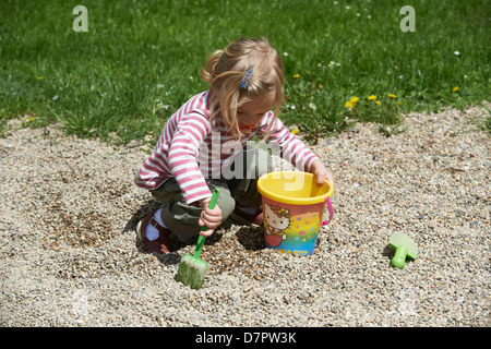 Blond blue eyes child baby girl two years old playing outdoor with stones and pebbles on playground Stock Photo