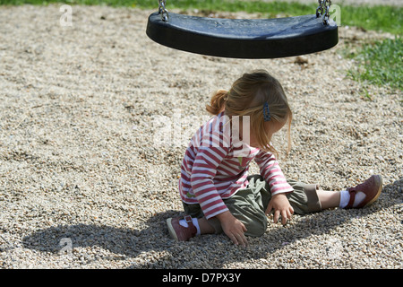 Blond blue eyes child baby girl two years old playing outdoor with stones and pebbles on playground Stock Photo