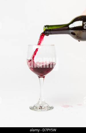 Red Wine pouring out of a bottle into a glass and splattering the white background. Stock Photo