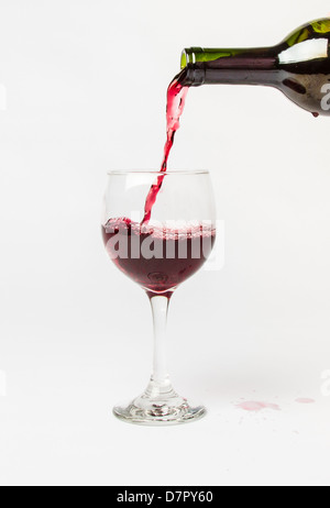 Red Wine pouring out of a bottle into a glass and splattering the white background. Stock Photo