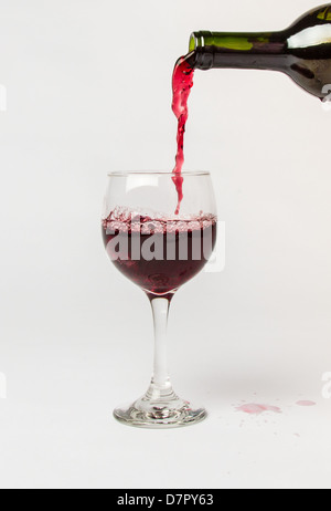 Red Wine pouring out of a bottle into a glass and splattering the white background. Stock Photo