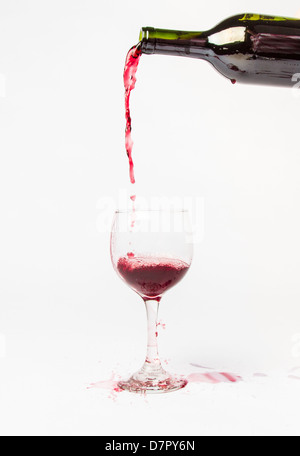 Red Wine pouring out of a bottle into a glass and splattering the white background. Stock Photo