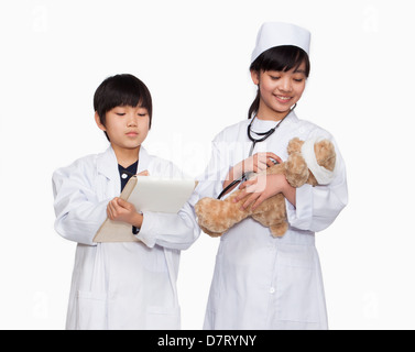 Boy and girl dressed up as doctors checking teddy bear's vital signs Stock Photo