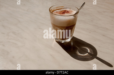 Caffe latte outdoors in a glass on a marble table. Sunshine and shadow. Stock Photo