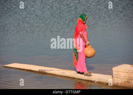 Indian woman in colorful sari carrying jar with water, Kitchan, Rajasthan, India Stock Photo