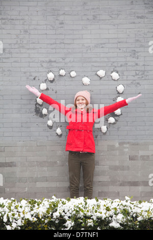 Young woman standing on wall with heart shaped snow balls Stock Photo