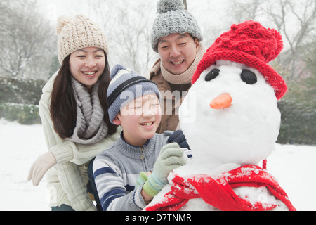 Family making snowman in a park in winter Stock Photo