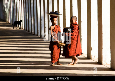 Novice Buddhist monks collecting alms, standing in the shadows of columns at Shwezigon Paya, Nyaung U, Bagan, Burma Stock Photo