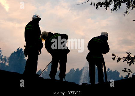 Smoldering remains of a ghetto house with a fireman spraying water firefighters extinguish a fire in an apartment house Stock Photo