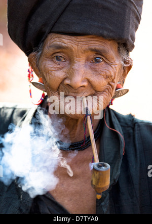 Woman of the Ann tribe in traditional black dress smoking a pipe outside a hill village near Kengtung, Shan State, Burma Stock Photo