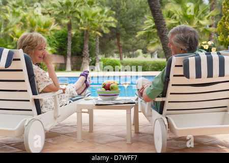 Elderly couple enjoying a glass of white wine on sun loungers by the pool Stock Photo