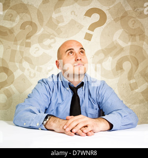 Businessman thinking and questioning, looking at question marks around his head. Stock Photo