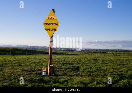 gas pipeline warning sign in a green field with houses in the distance. Stock Photo