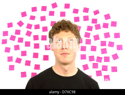 Young man with pink sticky notes and question marks thinking about decision making Stock Photo