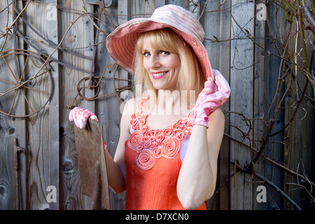 Attractive woman with gardening hat and gloves poses in front of old fence Stock Photo