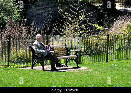 Single old man sitting on bench in a sunny park Stock Photo