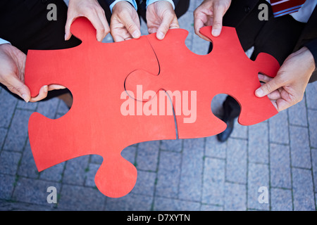 Many hands holding two red jigsaw puzzle pieces Stock Photo