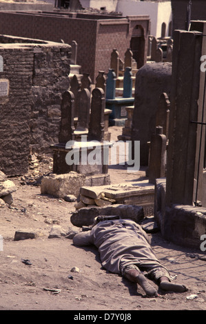 A homeless person sleeping in the ground amid dense grid of tomb and Islamic mausoleum structures in the City of the Dead or Cairo Necropolis where some people live in southeastern Cairo, Egypt. Stock Photo